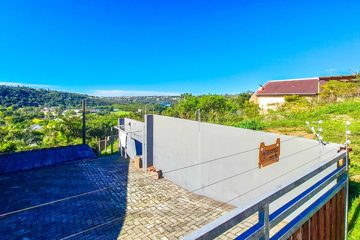 Rear exterior view featuring a paved driveway, boundary wall with electric fencing, and scenic hillside views.