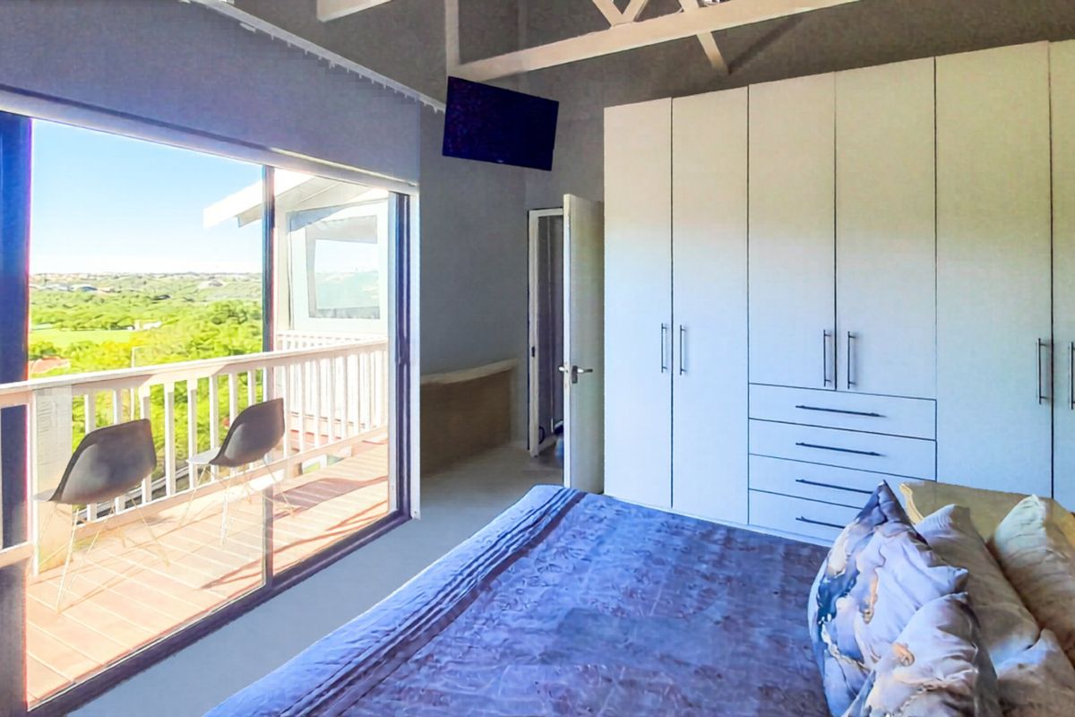 Spacious bedroom featuring built-in cupboards, exposed roof trusses, and a large sliding door opening onto a private balcony with scenic views.