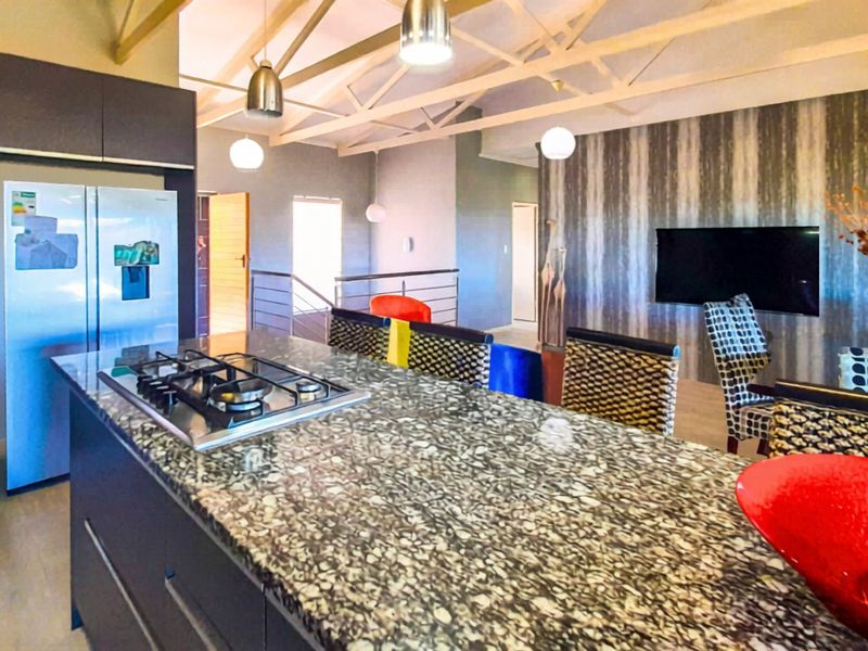 Spacious open-plan living area featuring a modern kitchen with a granite island, gas hob, and high exposed roof trusses.