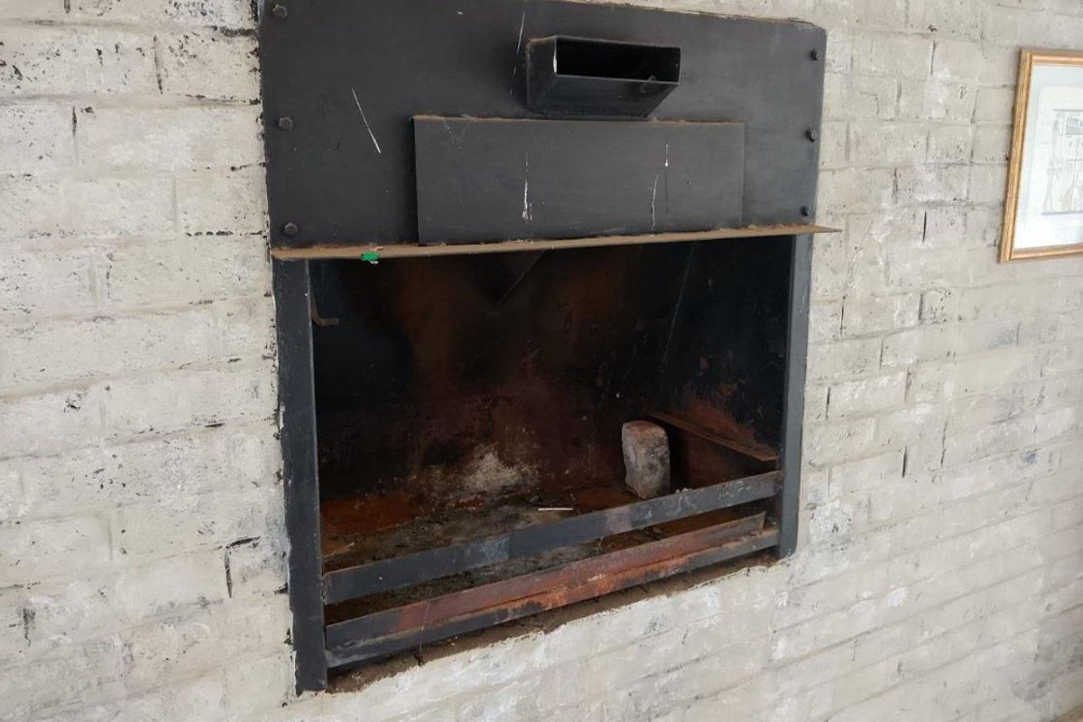 A close-up view of a built-in metal fireplace set into a painted brick wall, showing signs of wear and corrosion.