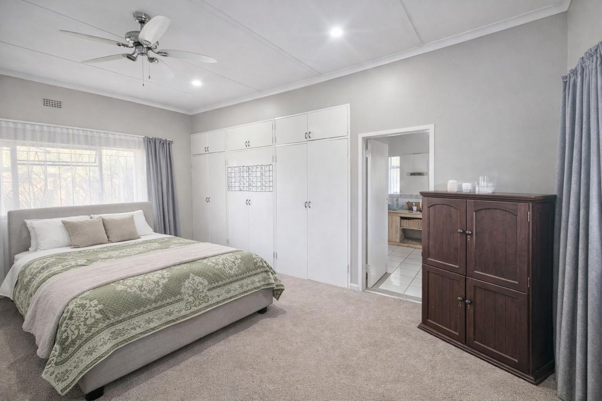 Spacious bedroom featuring neutral walls, carpeted flooring, ample built-in cupboard storage, and a ceiling fan, with an adjoining en-suite bathroom.
