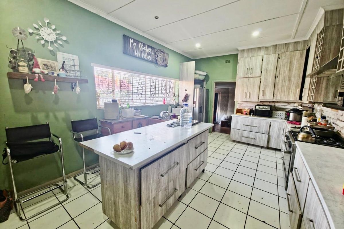 A functional kitchen featuring a central island, wood-look cabinetry, gas hob, and tiled flooring, offering a practical layout with potential for cosmetic updates.
