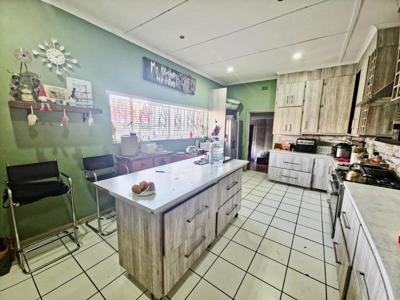 A functional kitchen featuring a central island, wood-look cabinetry, gas hob, and tiled flooring, offering a practical layout with potential for cosmetic updates.