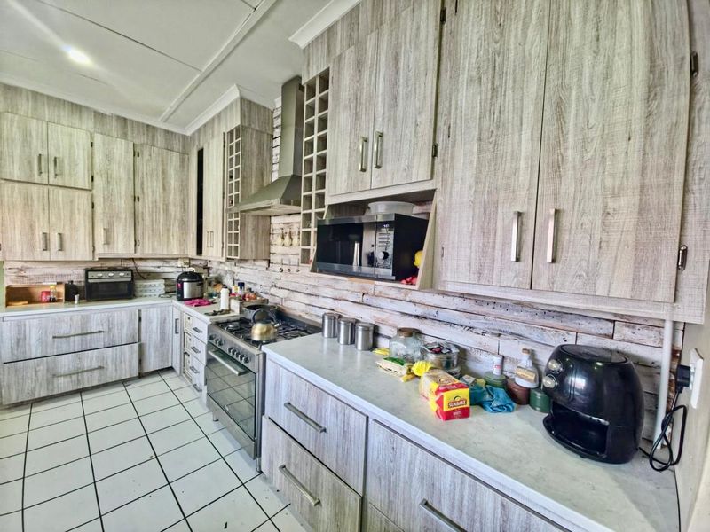 A functional kitchen featuring wood-look laminate cabinetry, a stainless steel gas stove with extractor fan, and tiled flooring.