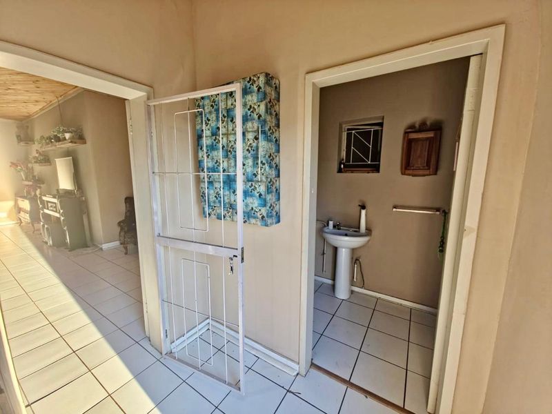 A hallway area featuring tiled flooring and access to a small bathroom with a pedestal sink.