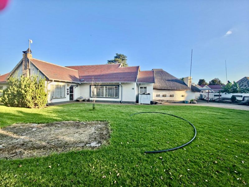 Rear view of a single-story house featuring a combination of tiled and thatched roofing, brick construction, and a spacious lawn area.
