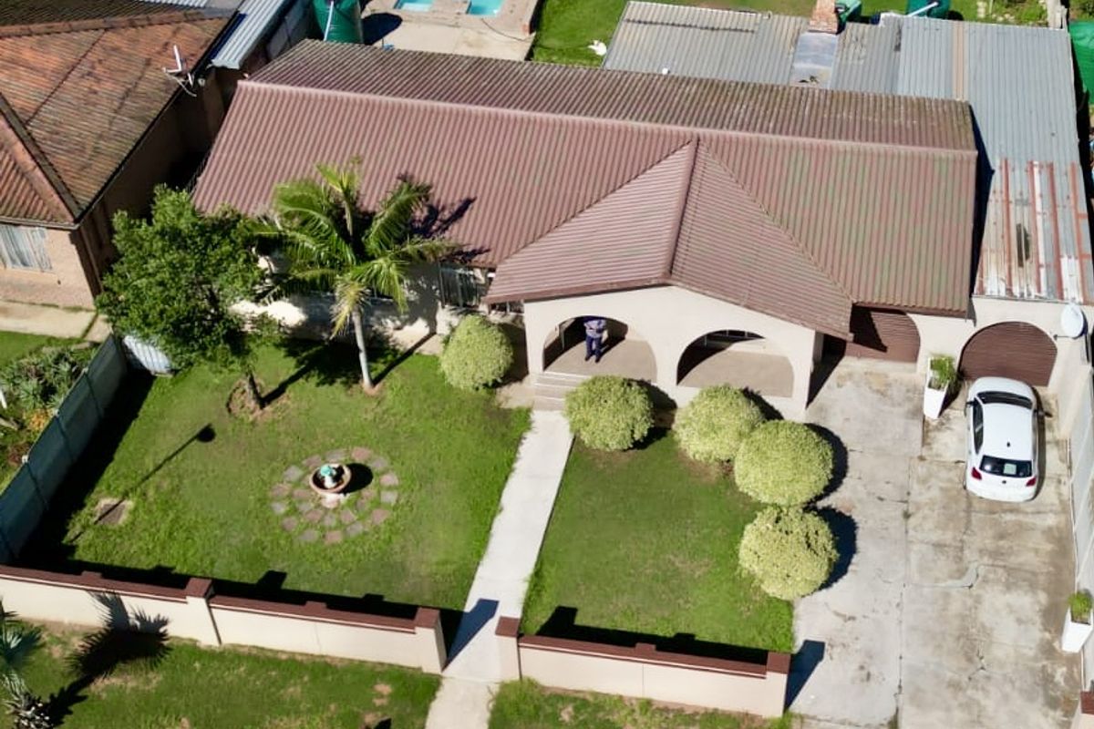 Aerial view of a residential property featuring a swimming pool, large garden, corrugated metal roof, and a concrete driveway with covered entrance.