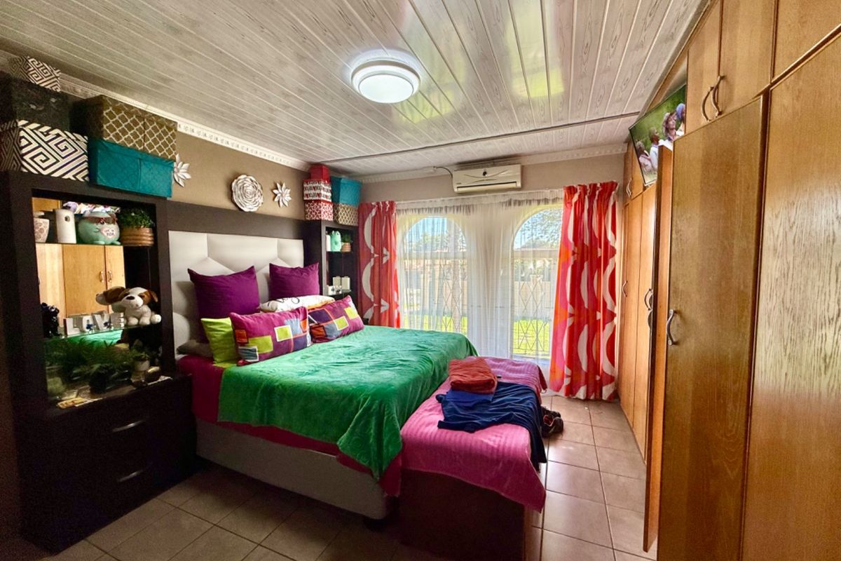A bedroom featuring built-in wooden cupboards, tiled flooring, an air conditioning unit, and arched windows with security bars.