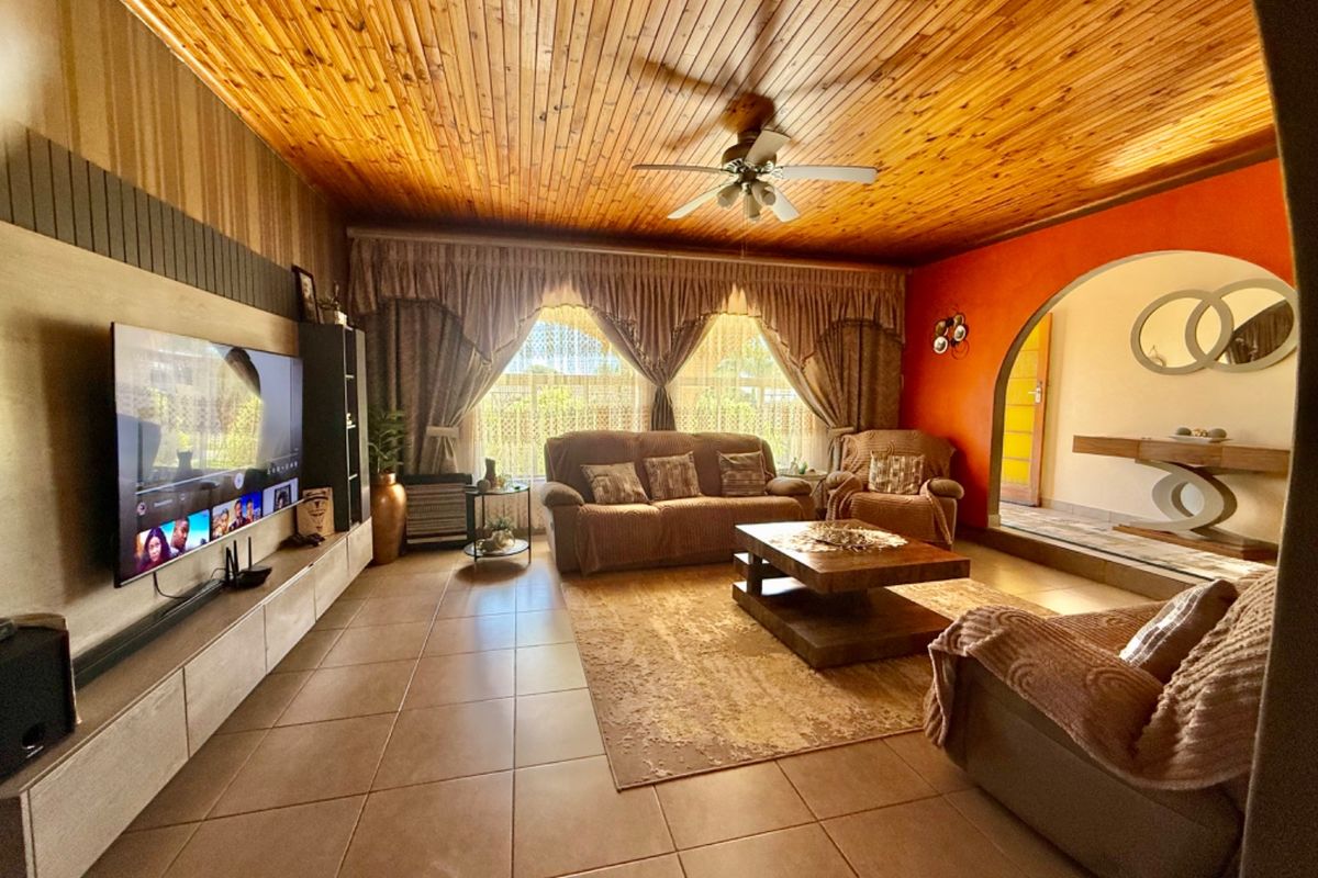 Spacious living room featuring a warm timber-clad ceiling, tiled flooring, and a distinctive arched entryway leading to the home's entrance.