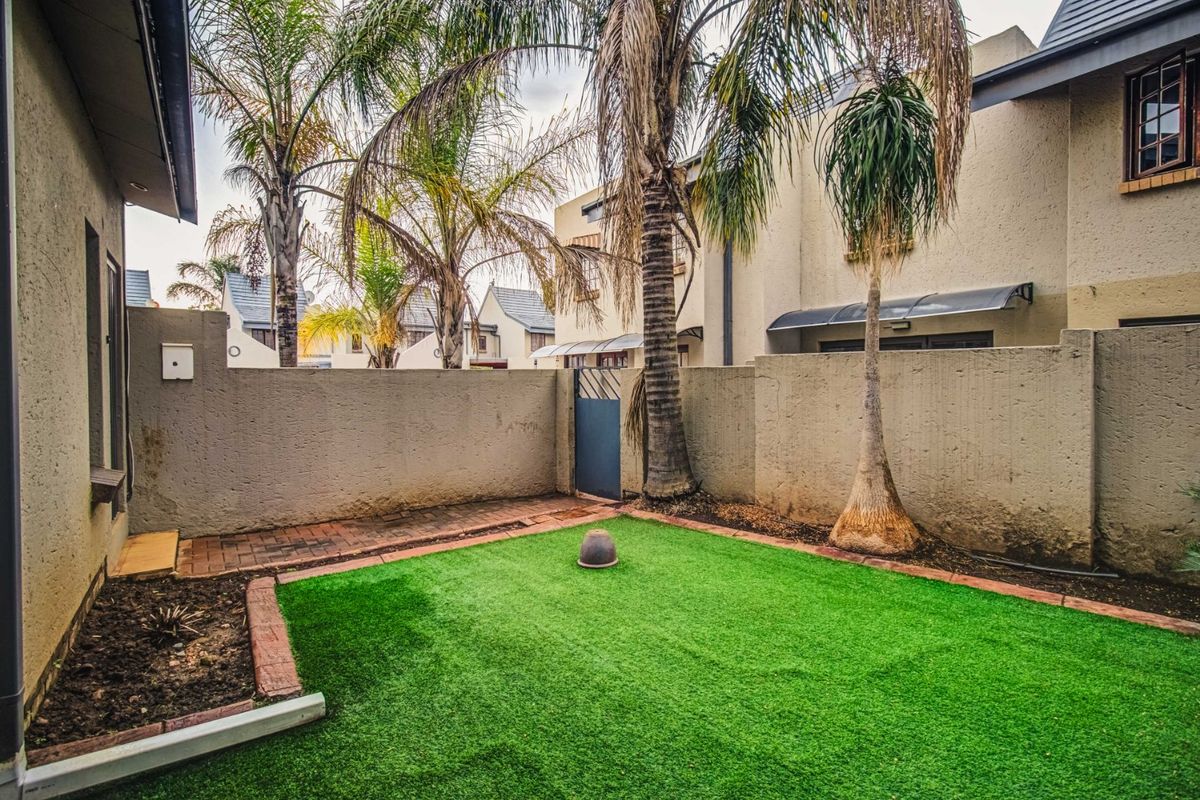 A private rear courtyard featuring an artificial lawn, brick-edged garden beds, and a secure boundary wall with a pedestrian gate.