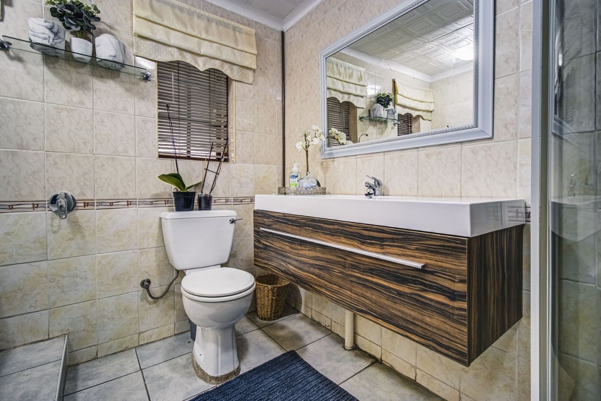 A functional bathroom featuring a modern wall-mounted vanity, ceramic basin, toilet, and fully tiled walls with a large framed mirror.