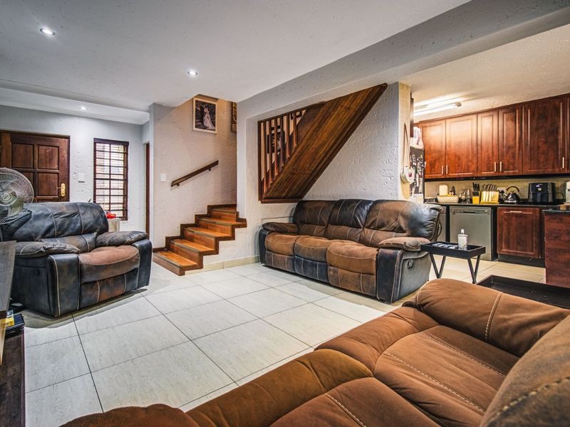 Open-plan living area featuring tiled floors, a wooden staircase with balustrade, and an adjacent kitchen with dark wood cabinetry.