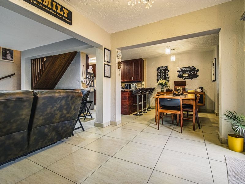 Open-plan living and dining area featuring tiled flooring, a wooden staircase, and a functional kitchen with a breakfast bar.
