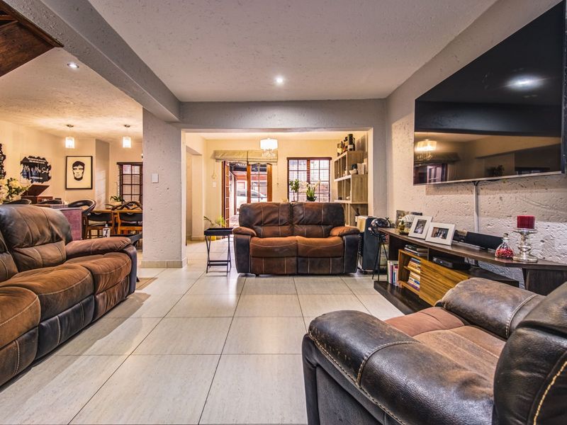 Spacious open-plan living area featuring tiled flooring, recessed lighting, and a textured wall finish, seamlessly connecting to the dining space and rear entrance.