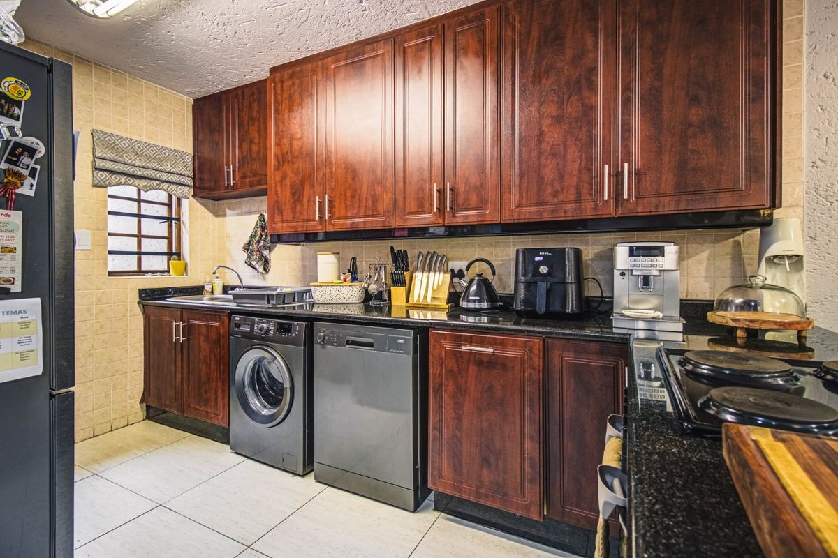 A functional kitchen featuring dark wood cabinetry, granite countertops, tiled backsplash, and integrated laundry and dishwasher appliances.
