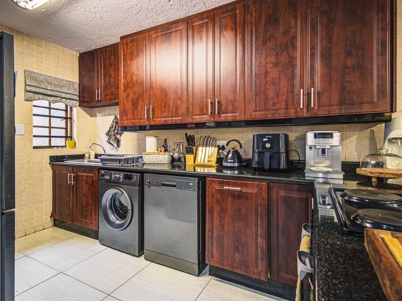 A functional kitchen featuring dark wood cabinetry, granite countertops, tiled backsplash, and integrated laundry and dishwasher appliances.