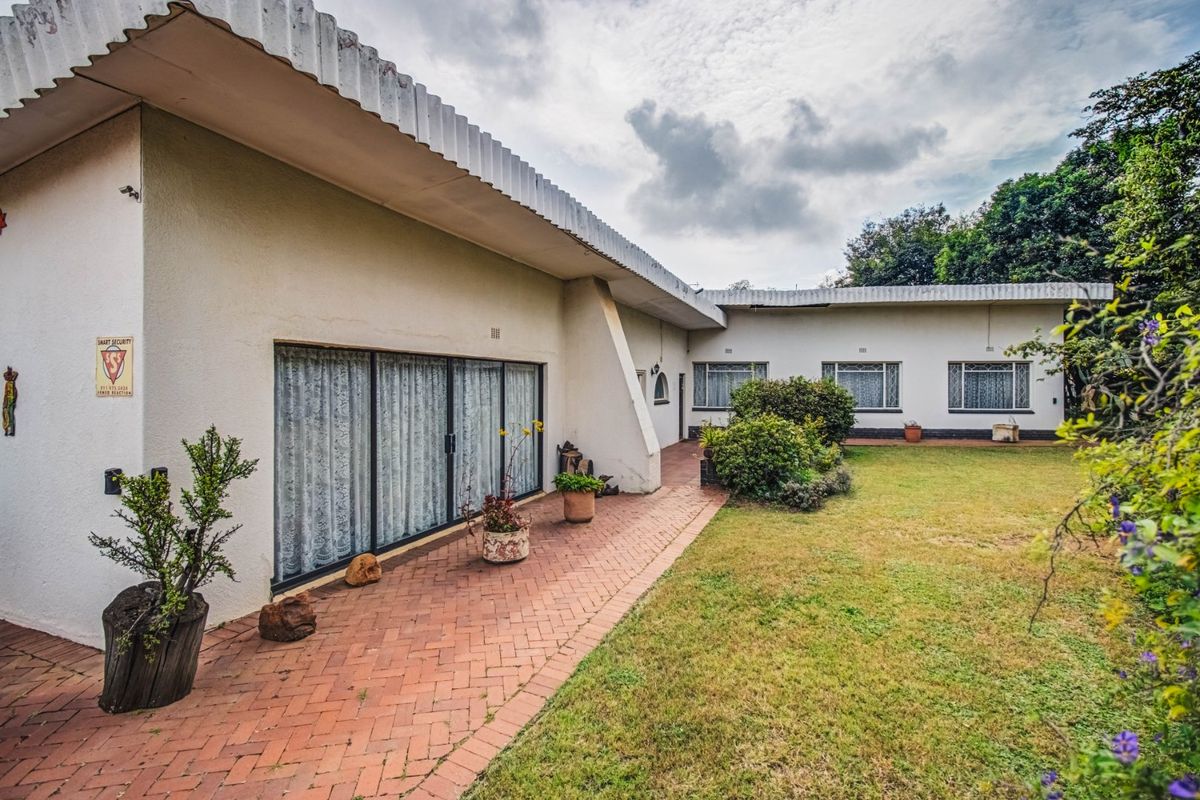 Rear view of the property featuring a brick paved patio, sliding glass doors, and a garden area with established landscaping.