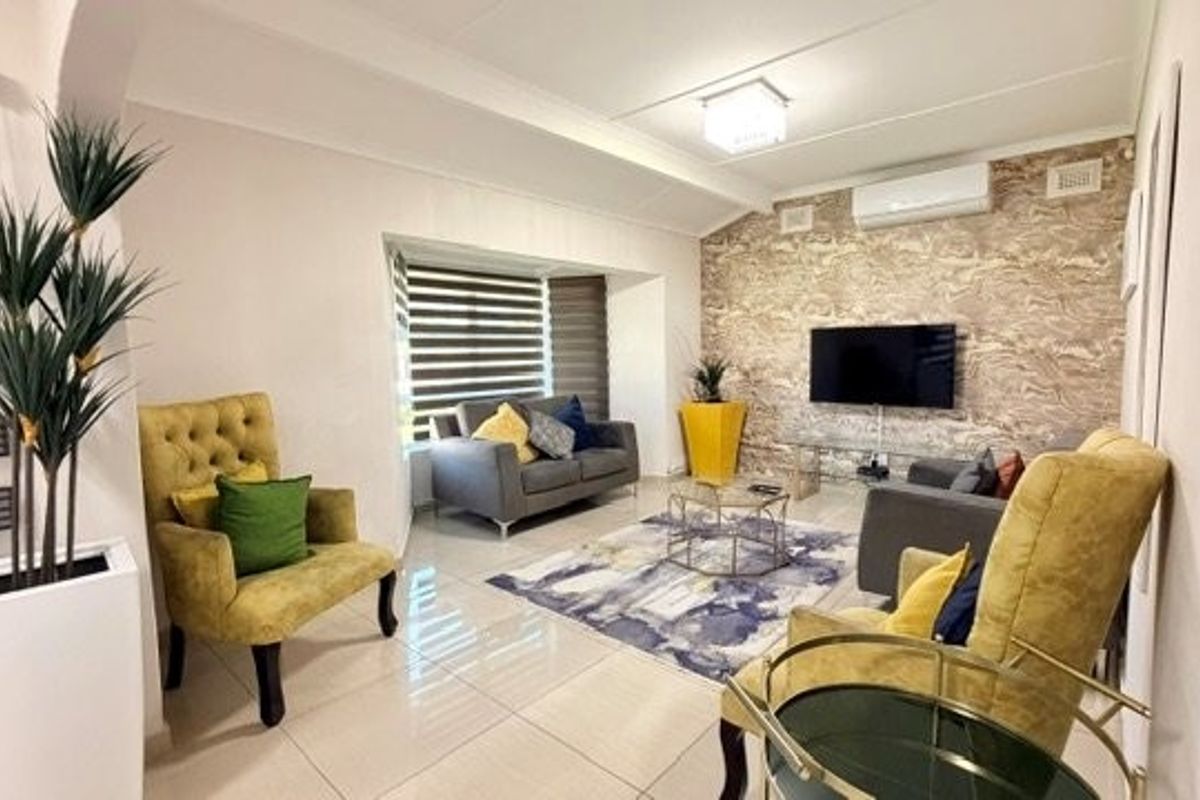 A well-maintained living room featuring polished tiled floors, a decorative feature wall, and a wall-mounted split-system air conditioner.