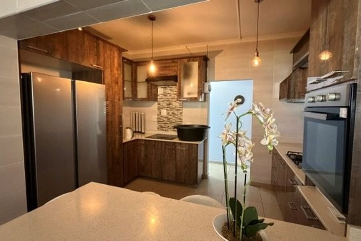 A functional kitchen featuring wood-finish cabinetry, stone countertops, integrated oven, hob, and extractor fan with modern pendant lighting.