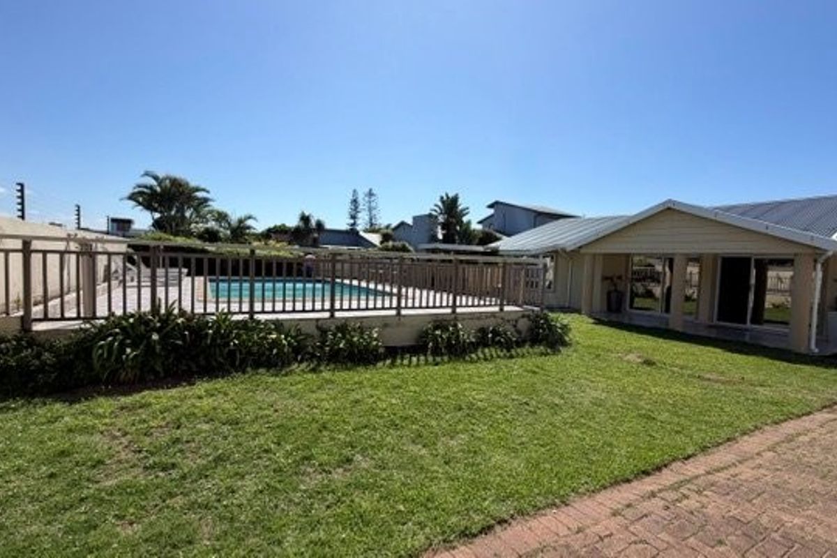 Rear exterior view featuring a swimming pool with safety fencing, a paved patio area, and a well-maintained lawn.