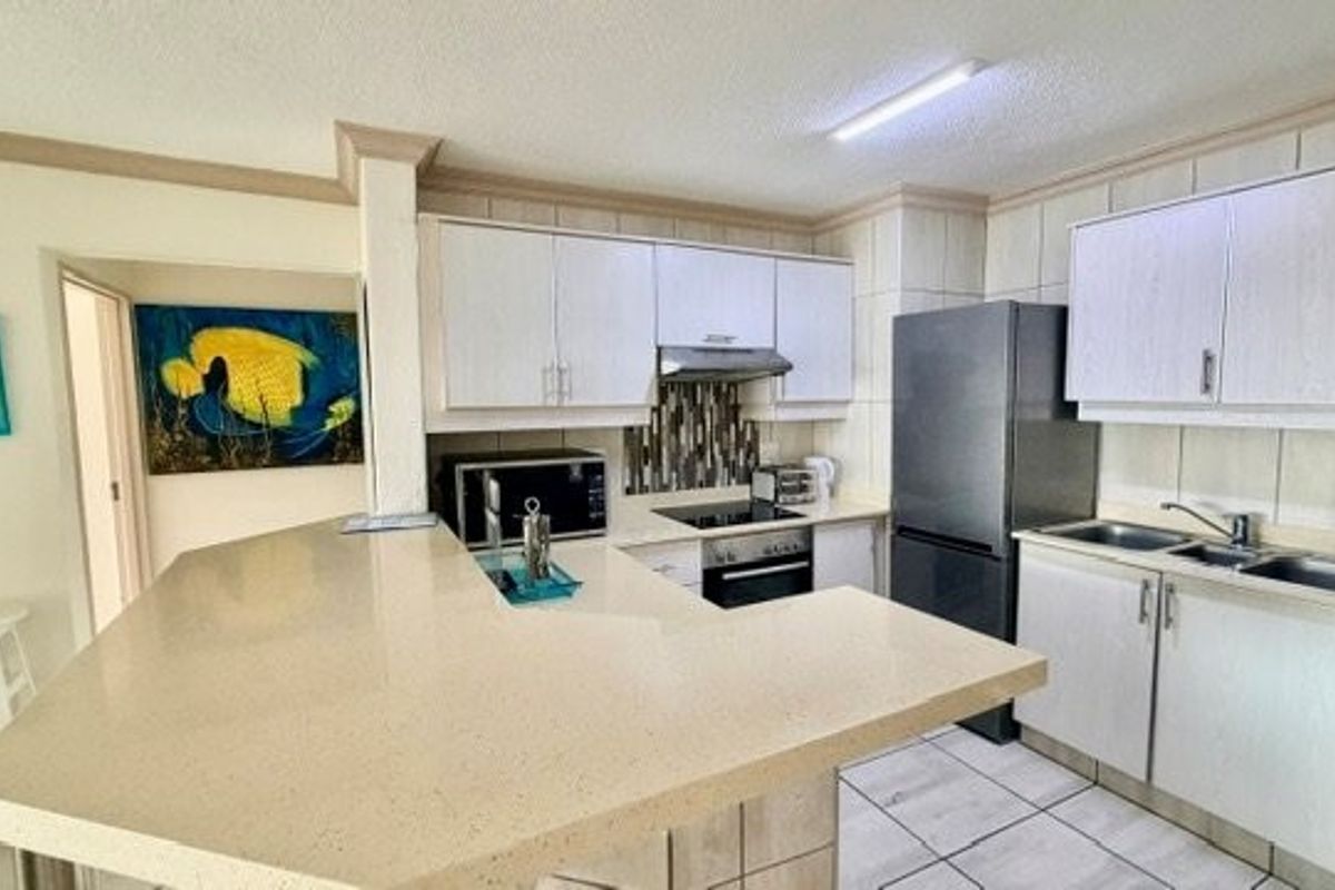 Functional kitchen featuring stone countertops, built-in cabinetry, electric hob, oven, extractor fan, and double basin sink with tiled backsplash.