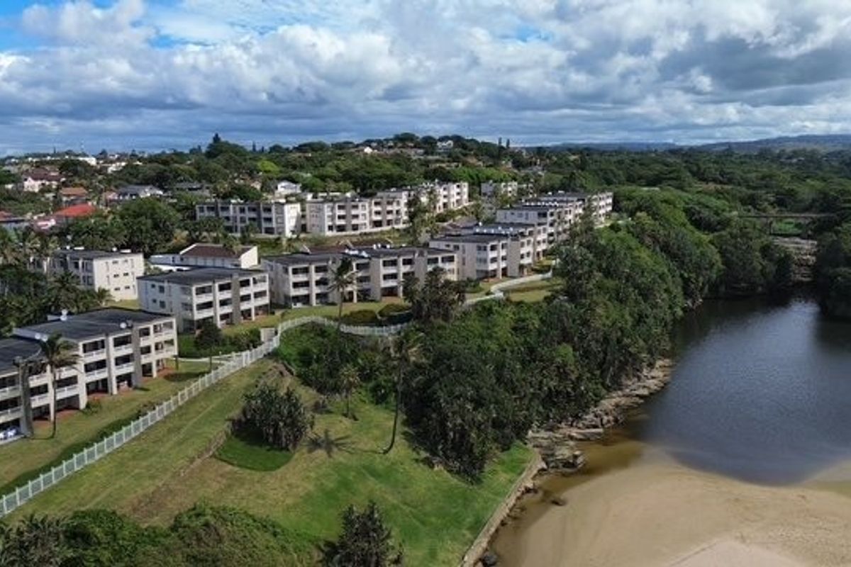 Aerial view of a residential apartment complex situated along a riverbank, featuring landscaped grounds and proximity to natural surroundings.