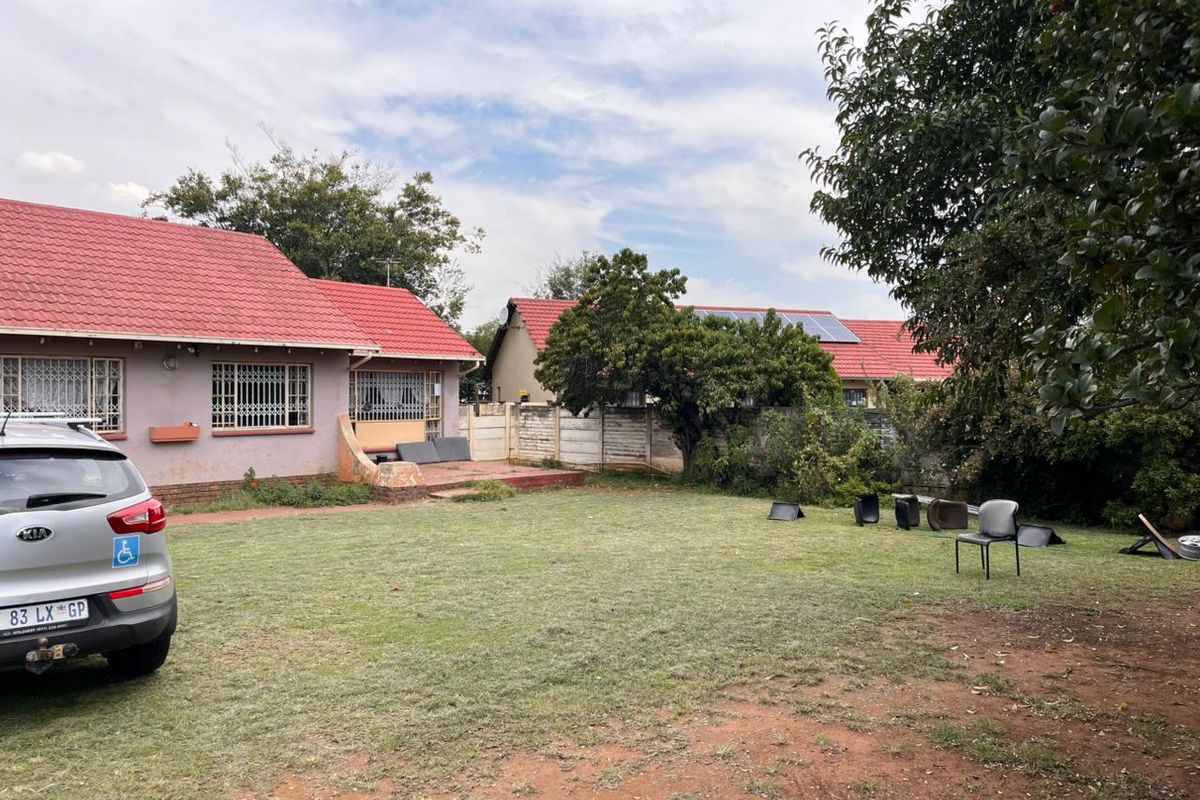A view of the rear garden and house exterior featuring a metal roof, security bars on windows, and a concrete boundary wall.