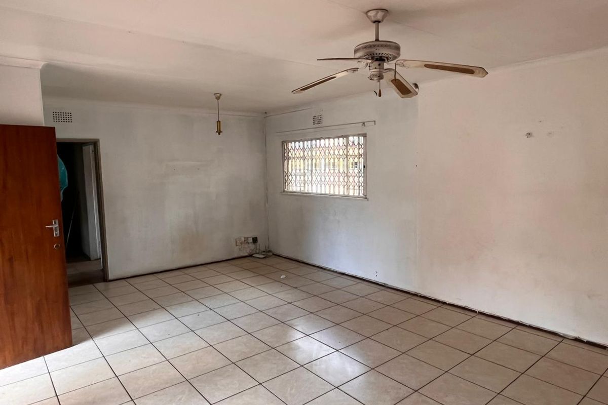 An empty living room featuring ceramic floor tiles, a ceiling fan, and a window with a security gate, ready for renovation or staging.