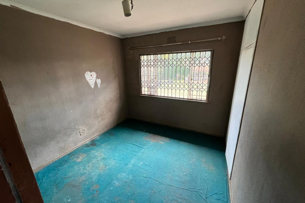 An empty bedroom featuring a built-in wardrobe, security gate on the window, and worn flooring, requiring cosmetic updates and refurbishment.