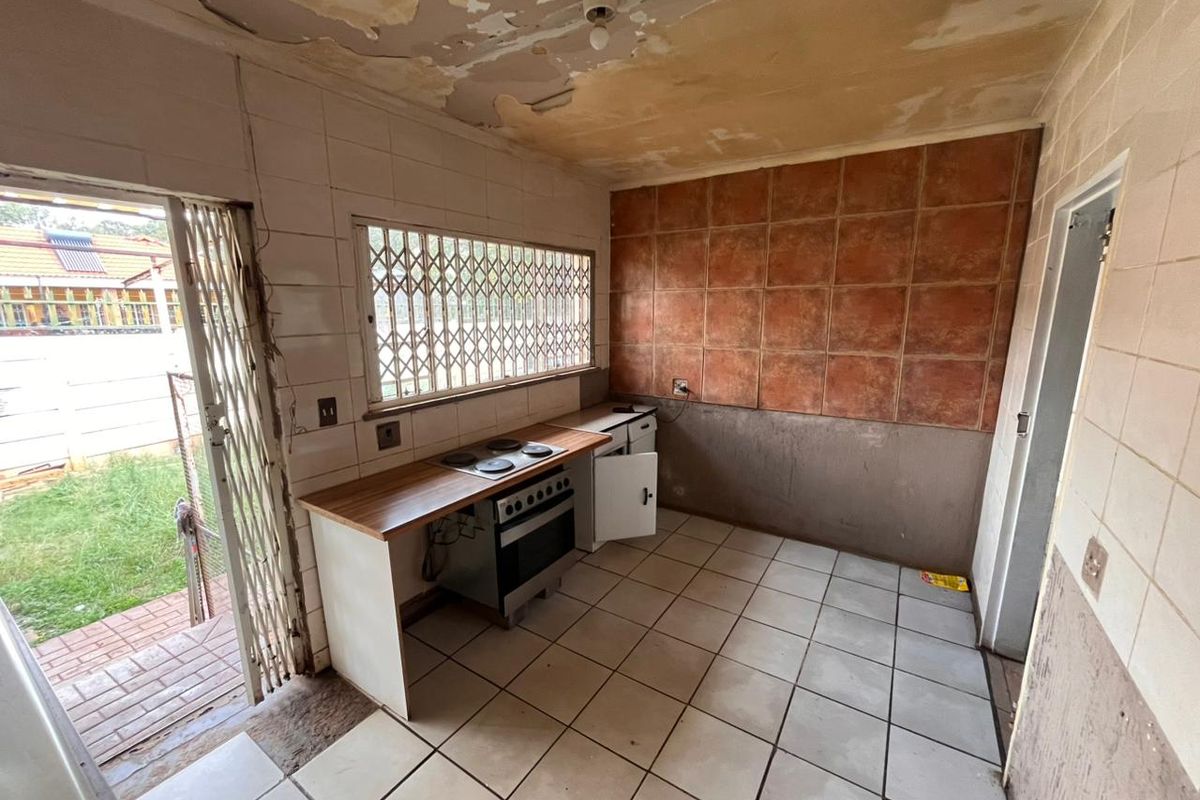 A dated kitchen space requiring renovation, featuring tiled flooring, a built-in stove, and direct access to the rear garden area.