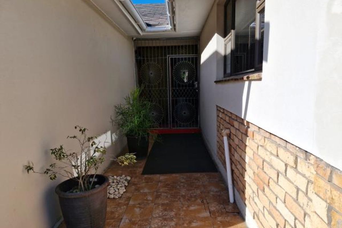 A narrow exterior side passage featuring tiled flooring, brick wall accents, and a secure metal gate entrance.