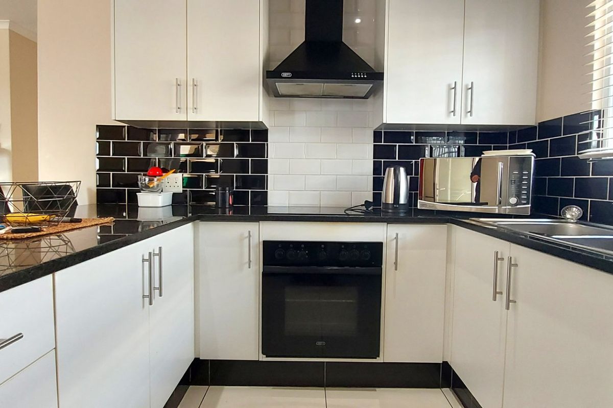 Modern kitchen featuring white cabinetry, contrasting black subway tile backsplash, granite countertops, and integrated stainless steel appliances.