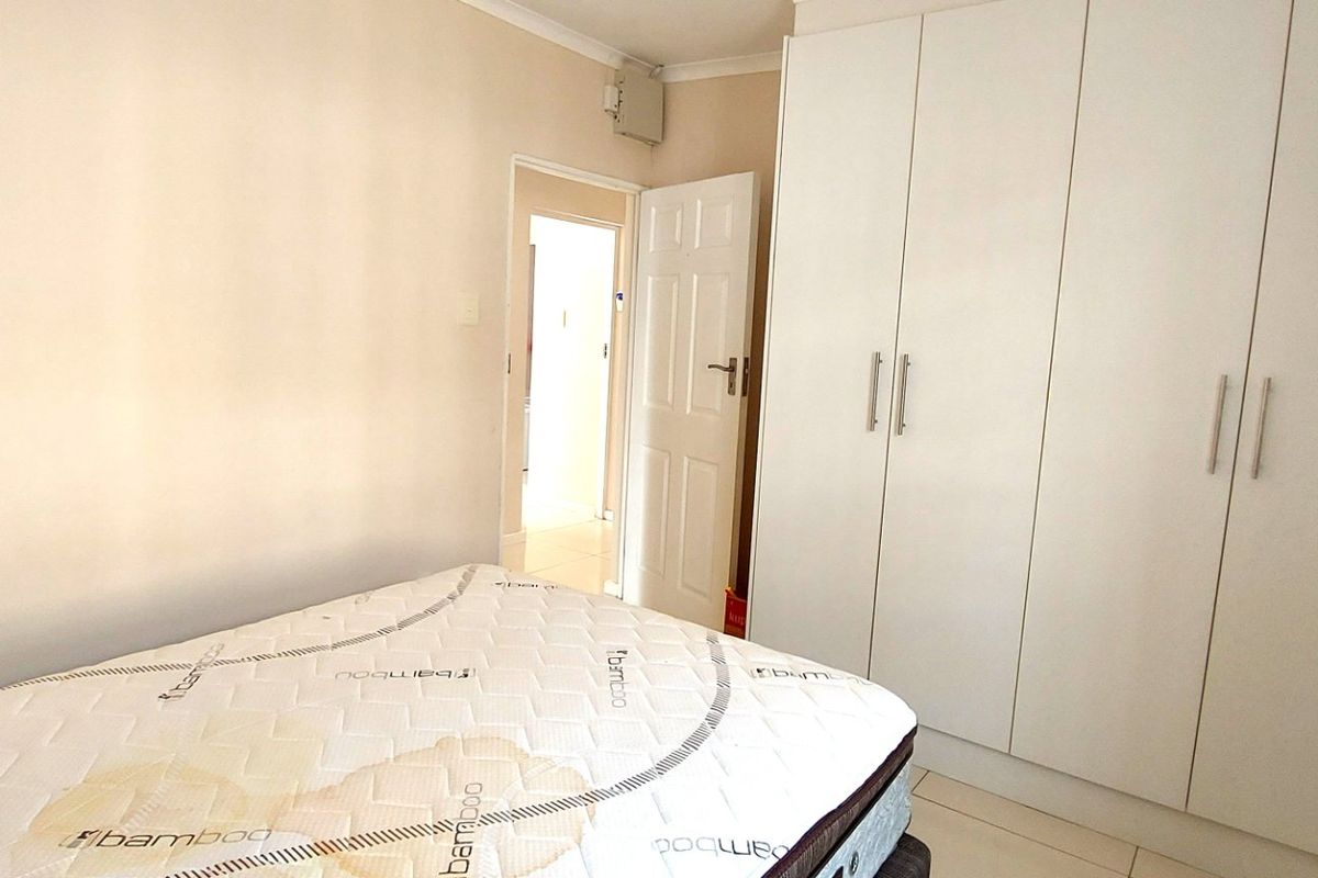 A bedroom featuring built-in cupboards, tiled flooring, and neutral wall finishes, providing a functional space with direct access to the hallway.