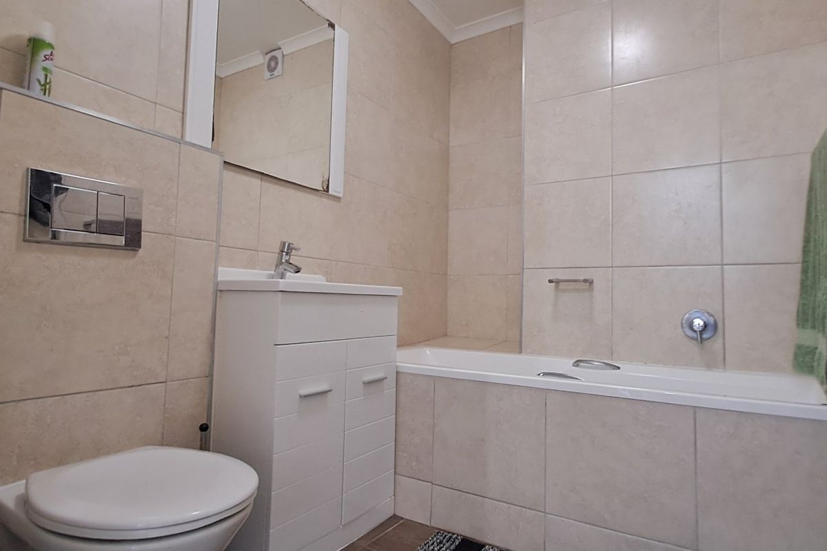 A functional bathroom featuring a wall-mounted toilet, vanity cabinet with basin, and a tiled bathtub area with neutral wall tiling.