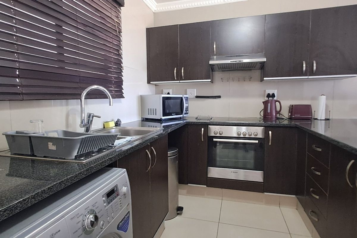 A functional kitchen featuring dark wood cabinetry, granite countertops, built-in oven, electric hob, extractor fan, and tiled flooring.