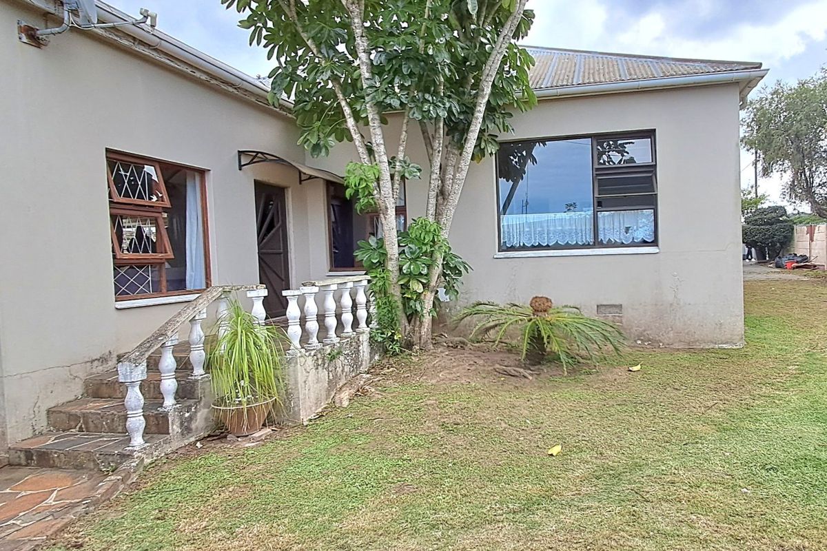Rear exterior view of the house featuring a small patio with concrete balustrades, stone steps, and established garden area.