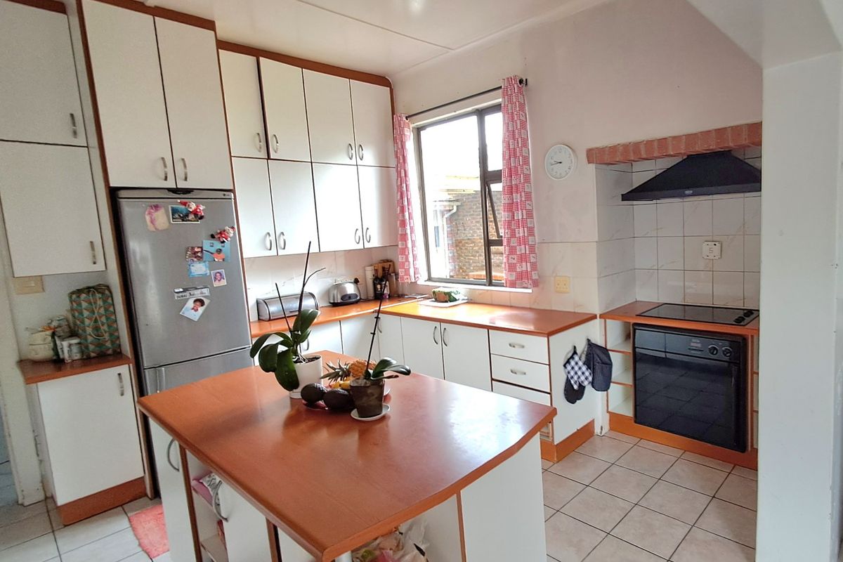 A functional kitchen featuring white cabinetry, laminate countertops, a central island, and built-in cooking appliances with tiled flooring.