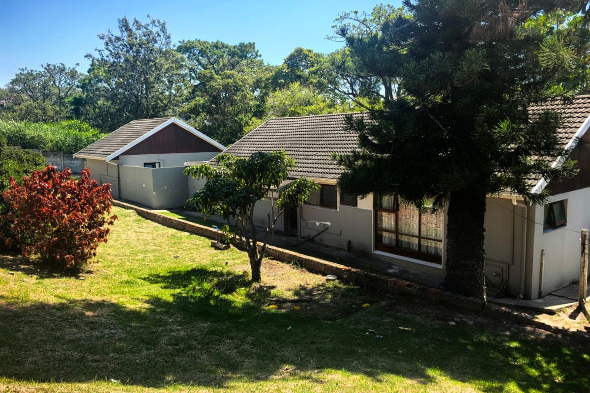 A view of the rear exterior of the house, featuring a tiled roof, large windows, and a spacious garden area with mature trees.