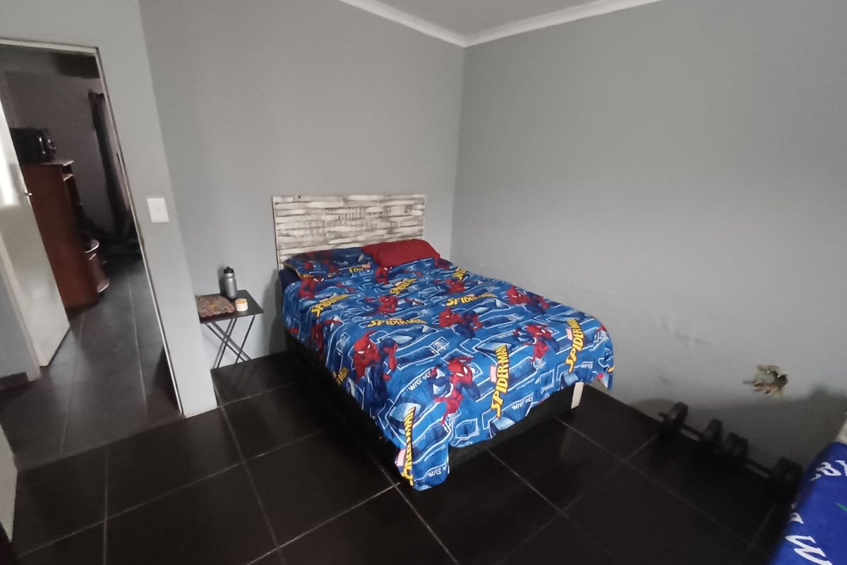 A bedroom featuring dark tiled flooring and neutral grey walls, requiring minor repairs to the wall surface.