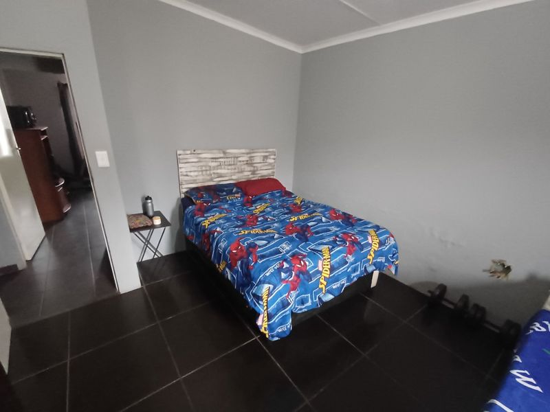 A bedroom featuring dark tiled flooring and neutral grey walls, requiring minor repairs to the wall surface.