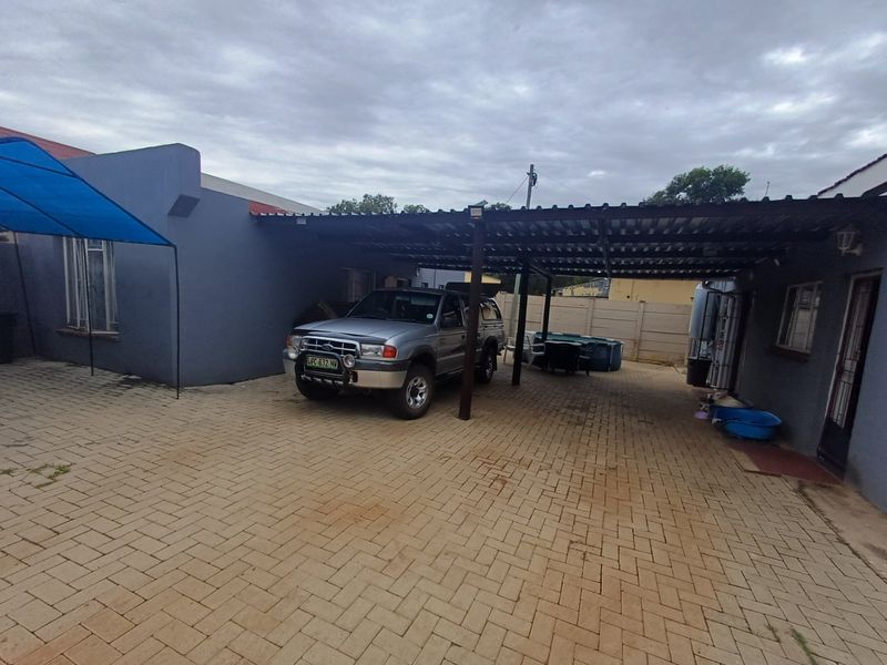 Rear exterior area featuring a paved driveway, a covered carport structure, and a precast concrete boundary wall.
