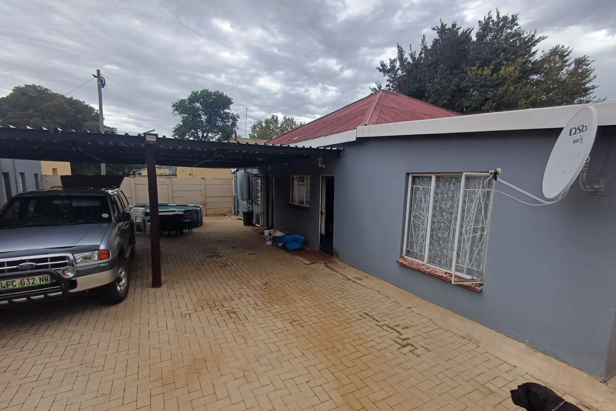 Rear exterior view of the property featuring a paved driveway, a covered carport area, and a corrugated metal roof.