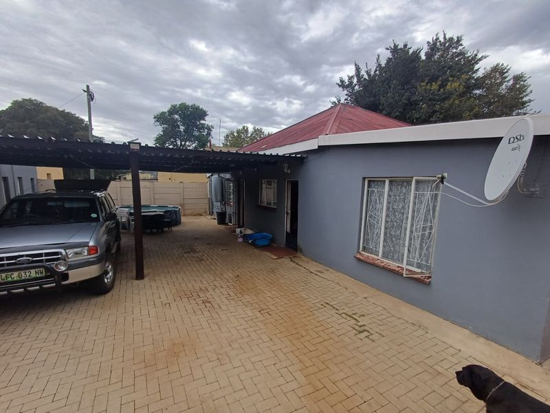 Rear exterior view of the property featuring a paved driveway, a covered carport area, and a corrugated metal roof.