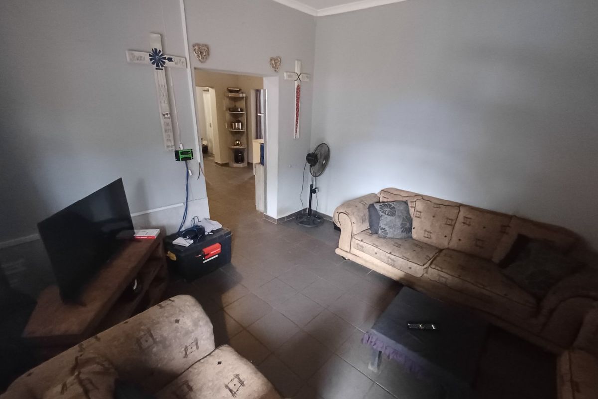 A living room featuring tiled flooring and coved ceilings, providing a functional space with direct access to an adjacent room.