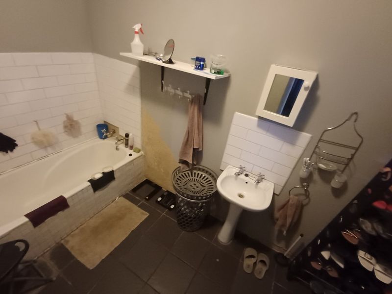 A functional bathroom featuring a bathtub, pedestal basin, and subway tile splashbacks, currently showing signs of wear and damaged wall finishes.