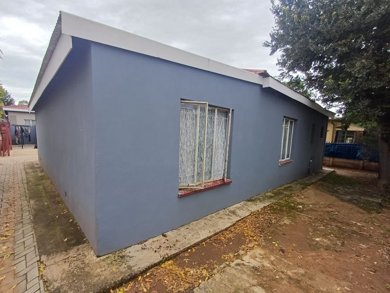 Side view of the house exterior featuring painted walls, metal security window bars, and a concrete apron pathway.