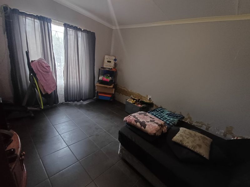 A bedroom featuring tiled flooring and a sliding glass door, currently showing signs of significant wall surface deterioration and dampness.