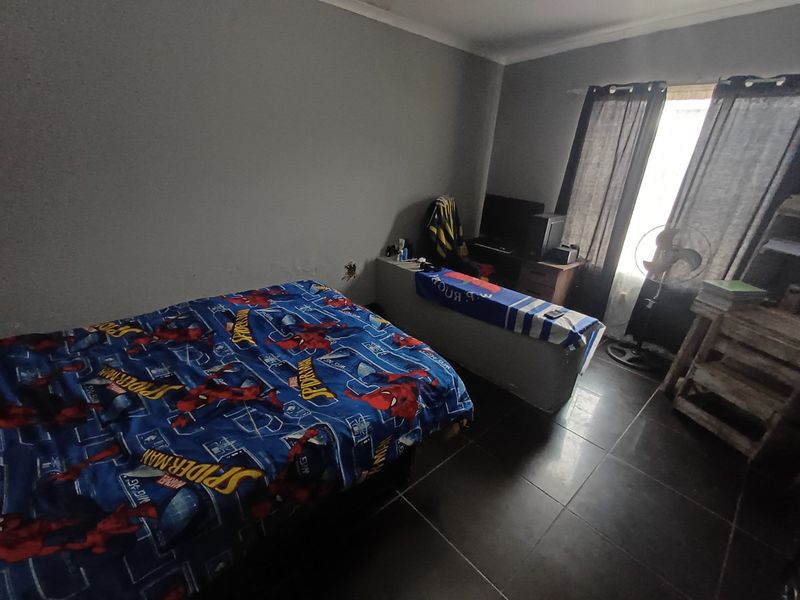 A bedroom featuring dark tiled flooring and natural light, currently requiring minor maintenance to address exposed electrical wiring on the wall.
