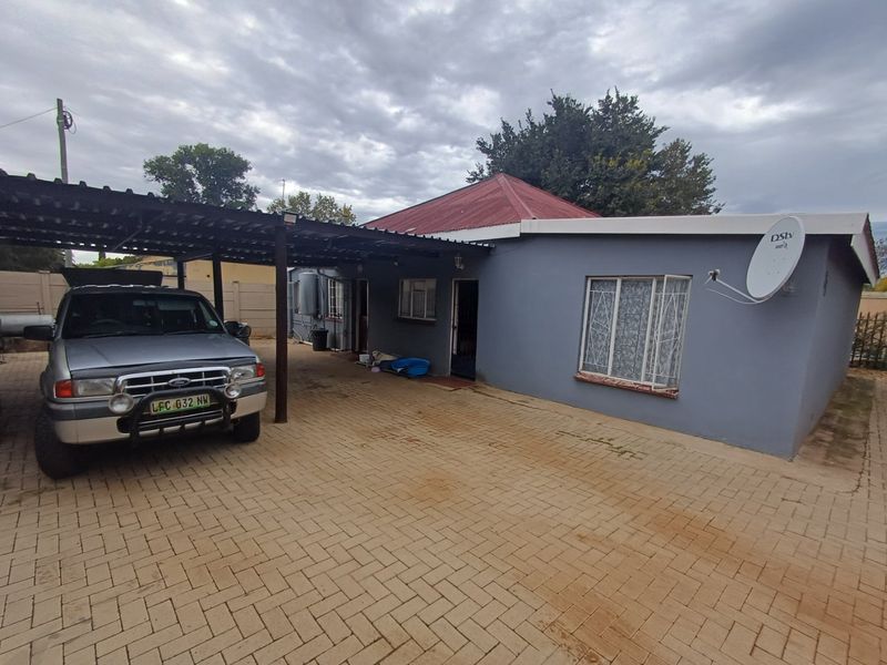Front exterior view of the house featuring a paved driveway, attached carport, and metal roof structure.