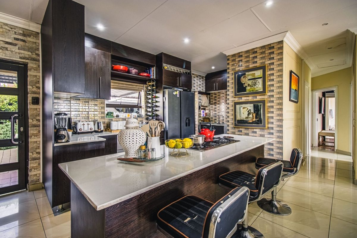 Modern kitchen featuring dark wood cabinetry, stone countertops, a central island with a built-in gas hob, and stylish brick-effect tiled feature walls.